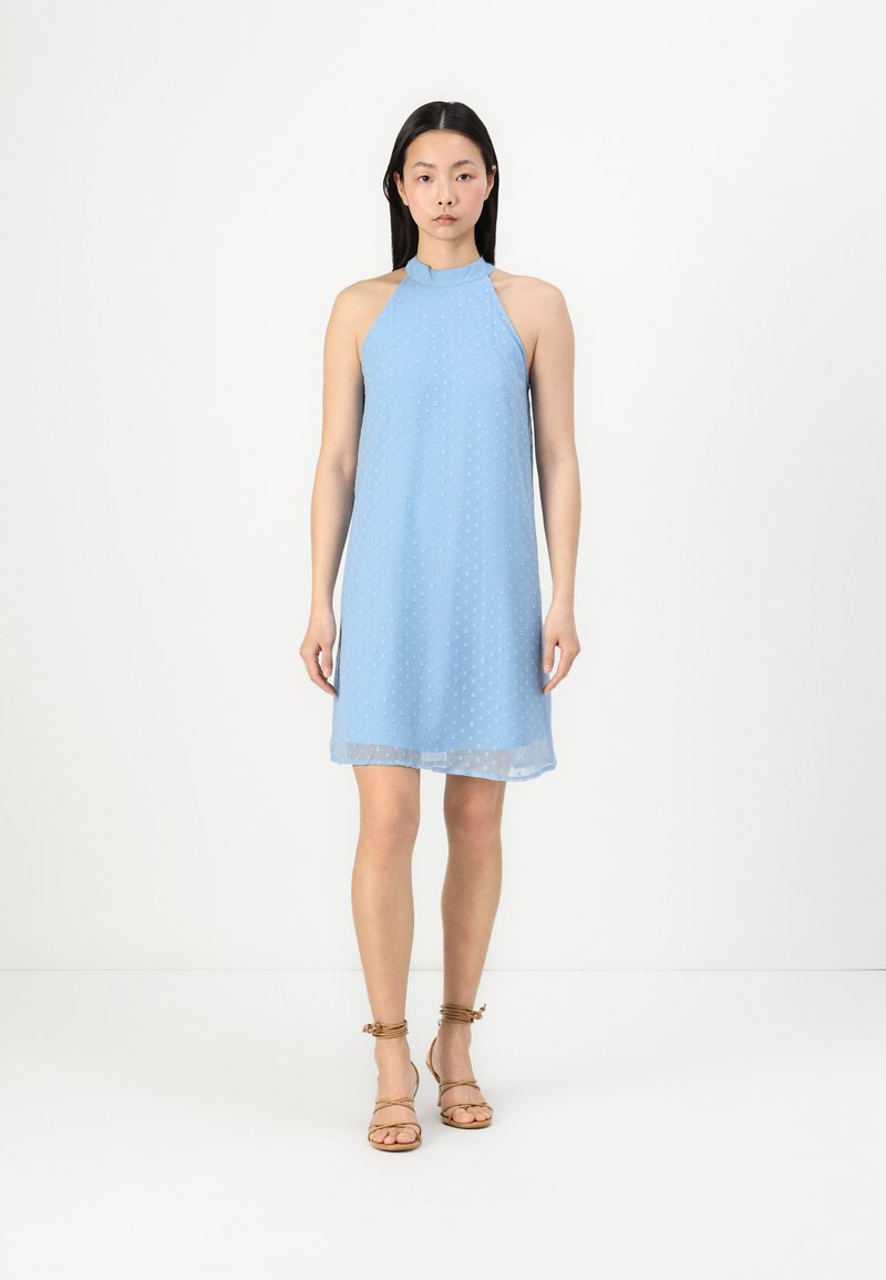 Light blue halter dress with a textured pattern of small dots, flowing fabric, and a mid-thigh length, paired with brown strappy sandals.