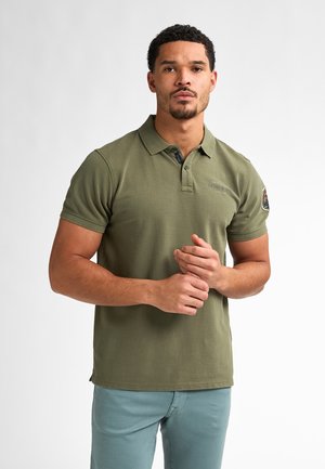 Polo olive en tissu coton avec un col à trois boutons, des manches courtes et un patch logo sur le bras supérieur. Design ajusté.