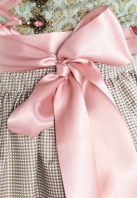 Nœud en satin rose noué autour d'une jupe à carreaux beige et blanc, avec un vêtement décoratif orné de fermoirs en or et bijoux roses au-dessus.