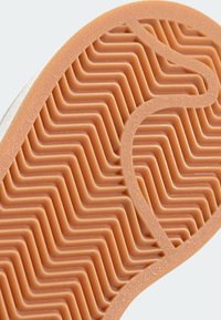 Suela de zapato de goma con un patrón de olas en textura naranja y un borde liso. El diseño curvado mejora la tracción y la flexibilidad.