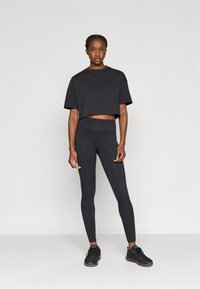 Μαύρο κοντό μπλουζάκι συνδυασμένο με μαύρο κολάν ψηλόμεσο. Το μοντέλο φοράει μαύρα αθλητικά παπούτσια. Λείο, ελαστικό ύφασμα με εφαρμοστό σχεδιασμό.