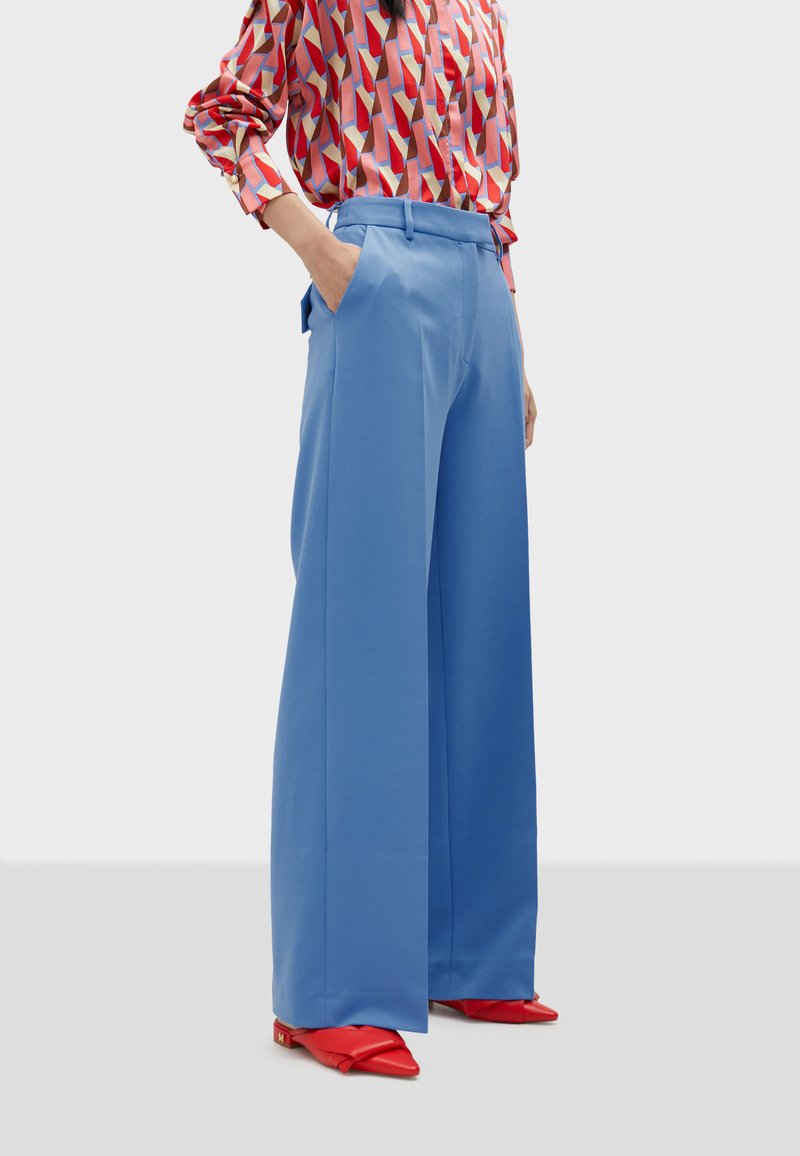 Light blue, wide-leg trousers with pockets and a smooth texture, paired with a patterned red and pink long-sleeve shirt and red pointed shoes.