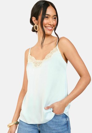 Top sin mangas de satén azul claro con encaje en el escote. Presenta tirantes finos y un corte relajado. Combinado con jeans de mezclilla y una pulsera llamativa.