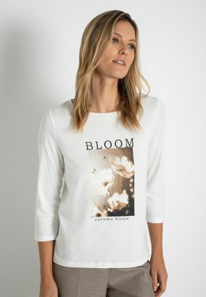 Witte lange mouwen T-shirt met bloemendessin en de tekst "BLOOM". Het ontwerp bevat een rechthoekig beeld van bloemen en een gestructureerde afwerking.