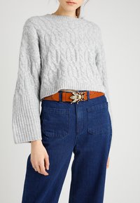 Light gray cable-knit sweater with wide ribbed cuffs, worn over dark blue high-waisted jeans and a brown belt featuring a decorative bee clasp.