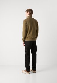 Oliven grønn fleecegenser med høy krage, kombinert med svarte bukser og sneakers med brune detaljer. Jevn tekstur og avslappet passform.