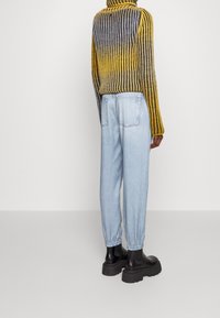 Strikket sweater med gul til grå gradient, ribbet tekstur; lyseblå tapered jeans med elastiske manchetter; sorte plateau støvler.