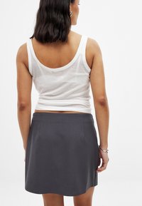 Jupe grise avec une texture lisse, présentant un design simple, de longueur mi-cuisse, et des poches latérales invisibles, portée avec un débardeur blanc.