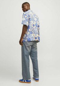 Korte mouwen shirt met een geometrisch patroon in blauw en crème, gecombineerd met lichte denim jeans en blauwe sneakers. Gladde stof en een relaxte pasvorm.