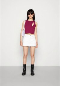 Top sem mangas cor bordeaux com recorte, combinado com uma saia mini de ganga branca e botas de tornozelo pretas. Os acessórios incluem uma pequena mala lilás.