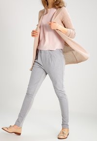 Light pink top paired with a textured beige cardigan, grey tapered pants, and nude loafers with decorative accents.