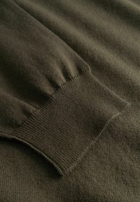 Gros plan d'une manche de pull en tricot vert olive foncé avec un poignet côtelé.