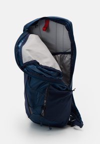 Zaino blu navy con apertura con cerniera, fodera grigia, tasca laterale in rete, spallacci regolabili e un gancio rosso sulla parte superiore.