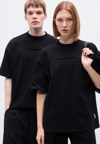 Μαύρα βαμβακερά T-shirts με στρογγυλή λαιμόκοψη, κοντά μανίκια και εκτύπωση κειμένου "BROKE SINCE MILANO" σε διακριτικό σχέδιο στο στήθος.