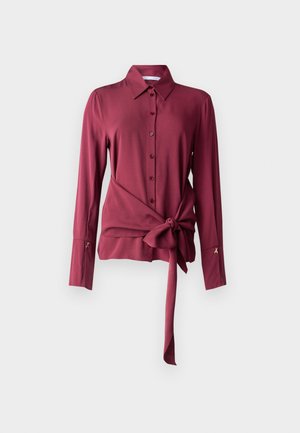 Burgunderfarget bluse laget av glatt stoff, med krage, knappefront, lange ermer og en knyttedesign i midjen. Gullfargede detaljer på ermene.
