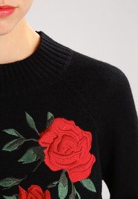 Czarny dziany sweter z okrągłym dekoltem, ozdobiony czerwonymi haftowanymi różami i zielonymi liśćmi. Teksturowany materiał z dopasowanym krojem.