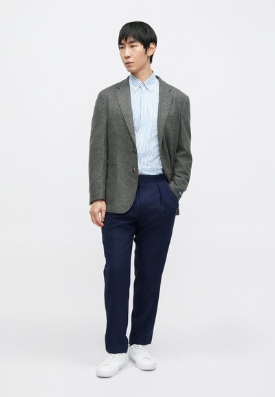 Blazer cinzento de lã, camisa às riscas brancas e azuis, calças azuis-marinho e ténis brancos. O blazer tem uma gola de lapela com entalhe e dois botões.