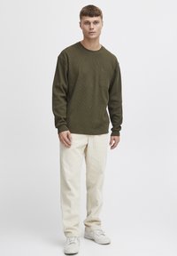 Langermet olivengrønn ribbestrikket skjorte med brystlomme, kombinert med off-white cordfløyelbukser og hvite joggesko.