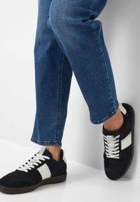 Sneaker in suede nero con dettagli in pelle bianca e lacci piatti. Indossati con jeans blu scuro, caratterizzati da una gamba dritta e un orlo accorciato.