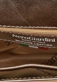 Interno di un articolo in pelle marrone che mostra l'etichetta cucita di NeroGiardini, il testo "fatto in Italia" e un piccolo dettaglio della bandiera italiana.