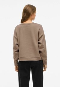 Brun sweatshirt med en avslappnad passform, rund halsringning och långa ärmar. Tyget verkar mjukt, med en något strukturerad yta och ribbad fåll.