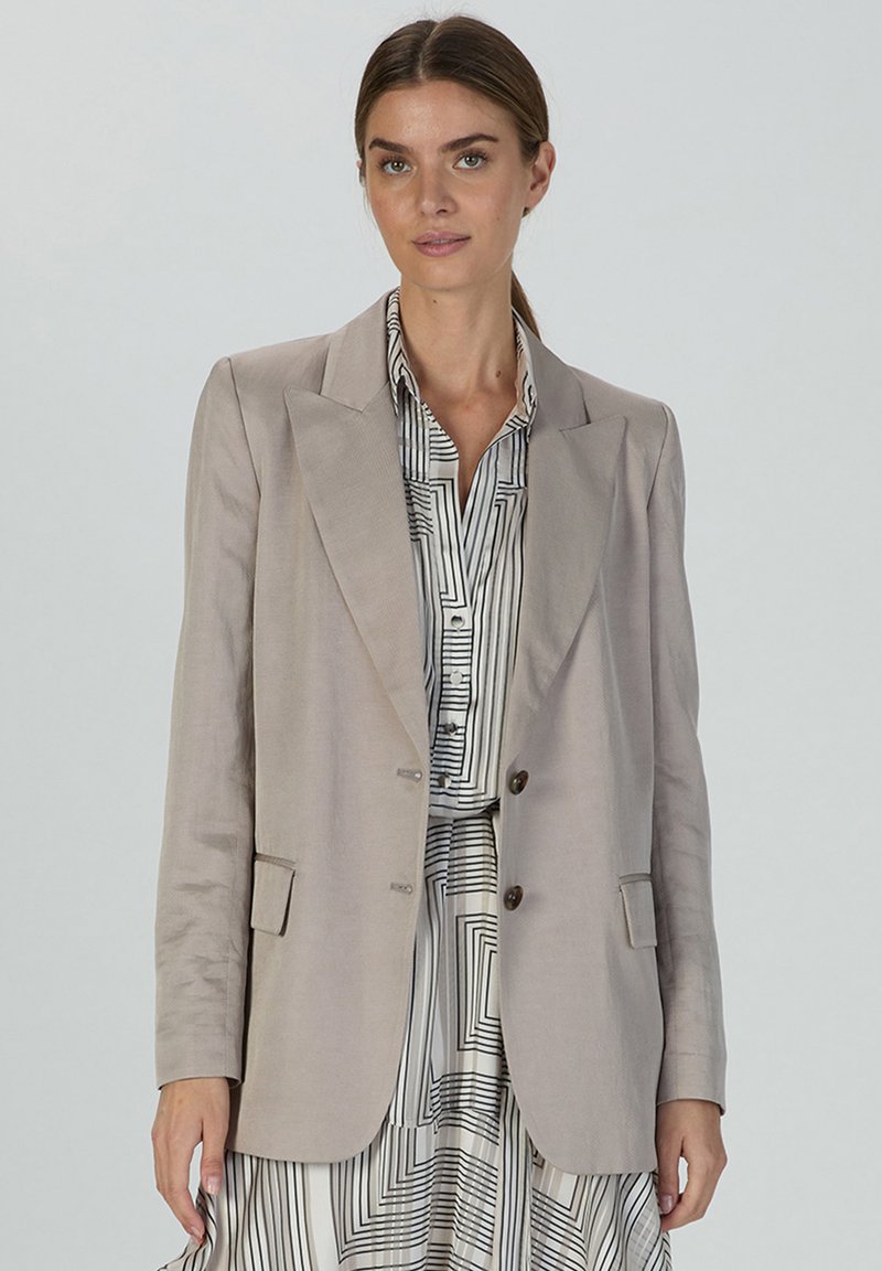 Hellbeige Blazer mit strukturiertem Design, spitzen Revers, zwei Knöpfen und seitlichen Taschen, kombiniert mit einer gestreiften Bluse. Glatte Textur.