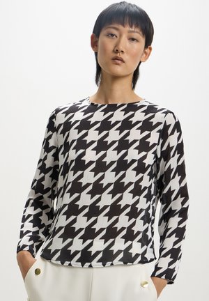 Blusa a fantasia houndstooth bianca e nera con maniche lunghe, scollo rotondo e tessuto leggero e testurizzato.