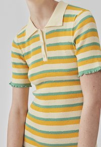 Polo rayé en tissu côtelé, présentant des rayures jaunes, vertes et crème, avec un col à revers et des manches courtes effilochées.