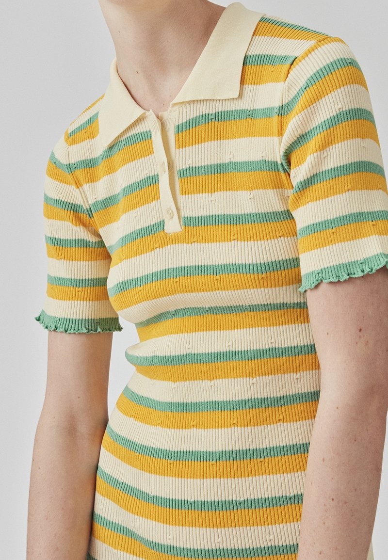 Polo rayé en tissu côtelé, présentant des rayures jaunes, vertes et crème, avec un col à revers et des manches courtes effilochées.