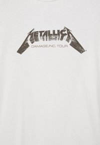 Chemise blanche avec logo Metallica noir usé et le texte "Damage, Inc. Tour" imprimé sous le logo au niveau de la poitrine.