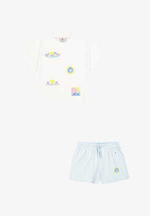 Camiseta de algodón blanca con estampados gráficos en tonos pastel y mangas enrolladas, combinada con pantalones cortos azul claro con cinturilla elástica y logo.