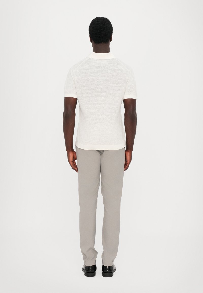 White short-sleeve polo shirt with textured fabric, paired with light gray trousers and black shoes, viewed from the back.