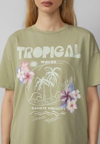 T-shirt en coton vert olive avec impression graphique représentant des palmiers, un soleil et des fleurs dans des tons roses et bleus. Coupe décontractée, col rond.