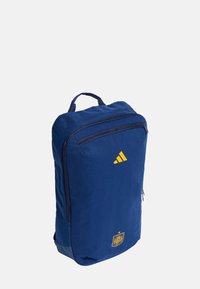 Mörkblå ryggsäck med en slät yta, med en framficka, gul Adidas-logotyp och ett spanskt emblem på botten.