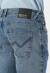 Vaqueros de denim en azul claro con una textura suave. Presentan una etiqueta de cuero negro y una distintiva costura en zigzag en el bolsillo trasero.