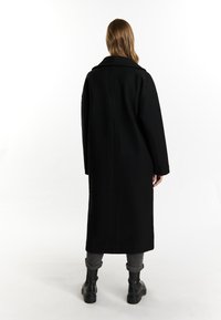 Dlouhý černý vlněný kabát se širokým límcem, oversize střihem a spadlými rameny. Záda mají čistý design bez ozdob.