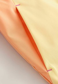 Zložena tkanina, ki prikazuje breskovo in bledo rumeno barvno polje z rožnatim šivom na gladki površini.