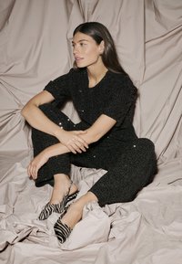 Completo nero con paillettes, maniche corte e pantaloni attillati, abbinato a scarpe con punta a strappo e tacco a zeppa con motivo zebra.