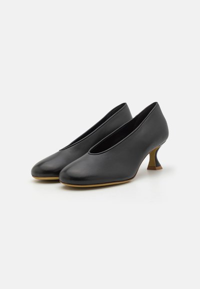 Sapatos de salto em pele preta com bico arredondado, design de corte baixo e um salto esculpido único. Textura suave com um brilho sutil.