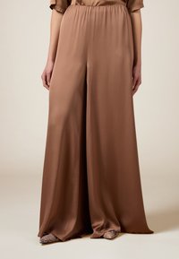 Pantalons amples marron en tissu satiné lisse avec une taille élastique. Notables pour leur design minimaliste et leur drapé élégant.