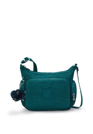 Teal crossbody bag with front and side zip pockets, adjustable strap, and a small black plush monkey keychain attached to the left side.