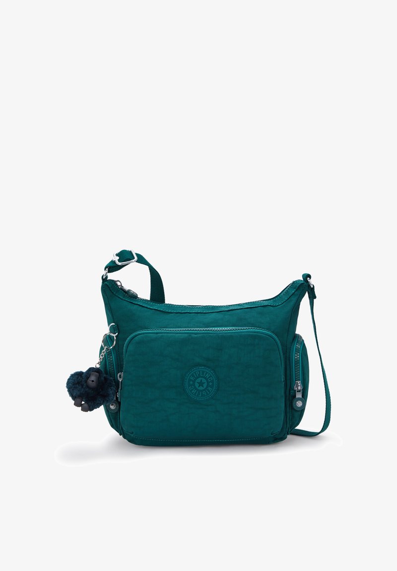 Teal crossbody bag with front and side zip pockets, adjustable strap, and a small black plush monkey keychain attached to the left side.