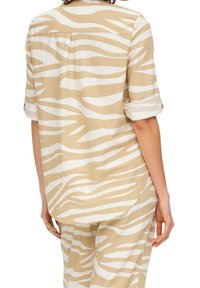 Camicia a righe beige e bianca realizzata in tessuto morbido, con una vestibilità ampia, maniche corte arrotolate e una piega sul retro.