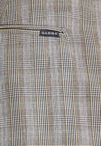 Grå och vit rutigt tyg med houndstooth-mönster, med inslag av guld och blått. Inkluderar en svart GABBA-etikett.