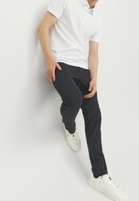 Vit polotröja, marinblå byxor och vita sneakers. Polotröjan har krage och korta ärmar; byxorna är slim-fit med en slät textur.