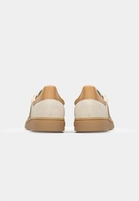 Sneakers ar beigu zamšādas virsotni un gaiši brūniem ādas papēža akcentiem. Izcils teksturēts gumijas zole un saistīšanas priekšpuse.