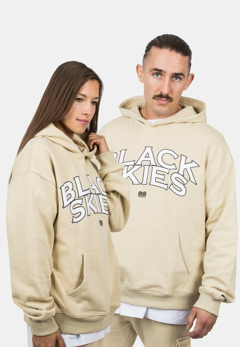 Bežové mikiny s tučným čiernym písmom "BLACK SKIES", vyrobené z mäkkého materiálu, s klokankovými vreckami a ribbovanými manžetami.