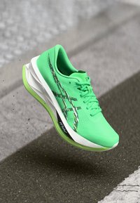 Grüner Sportschuh mit einem atmungsaktiven Obermaterial, gemusterten Akzenten und weißer Sohle. Verfügt über Schnürsenkel, verstärkte Zehenpartie und Logodetails.