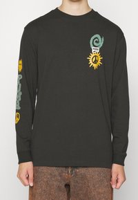 Long-sleeve black T-shirt made of cotton with colorful graphic designs, including a swirl, sun, peace symbol, and "PUMA" text on the sleeves.