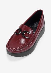 Mocasines de cuero burdeos sin cordones con un acabado texturizado y un detalle de cadena negra, que cuentan con una suela de plataforma gruesa para añadir altura.